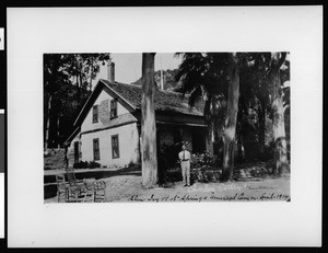 Exterior view of the Glen Ivy Hot Springs Hotel, showing a man and chairs in the foreground, April 1914