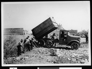 Dump truck offloading, showing group of workers nearby