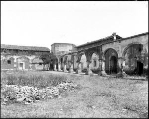View from the quadrangle of Mission San Juan Capistrano, showing the surrounding arcade and nearby buildings, Orange County, California, ca.1900