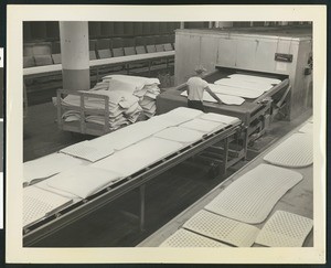 Worker placing white rubber mats into a machine, ca.1945