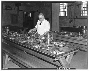 A man setting dinner places for inmates (presumably at Terminal Island Federal Prison)