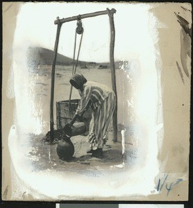 Woman taking water from a well, ca.1900