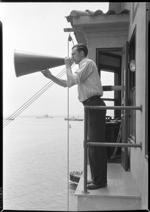 Man standing outside of the Marine Exchange as he yells through a megaphone, 1936