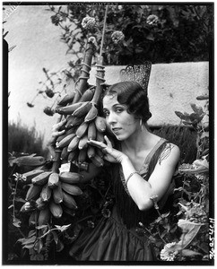 Portrait of a woman in flapper-style clothes posing with a bunch of bananas, 1929