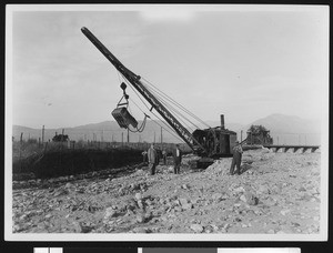 Seven men posing next to a crane helping flood control in Pomona, ca.1920