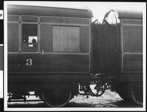 Two connected railway cars, showing passengers through a window at left, ca.1930