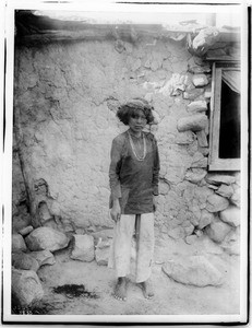 Navajo Indian boy standing in front of an adobe dwelling, ca.1901