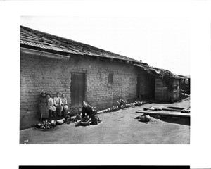 Indian woman grinding corn while children watch at the Hacienda Aguilar, ca.1899