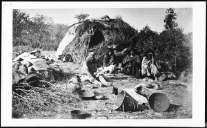 Exterior view of an Apache Indian home in Arizona with five Indians sitting outside, ca.1884