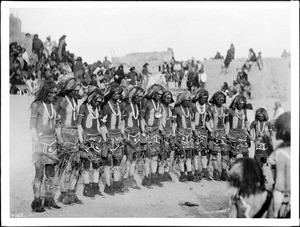 Line of a dozen Hopi snake priests singing songs and prayers before the kiva or kisi at the pueblo of Oraibi, Arizona, 1898