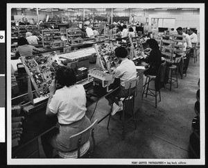 Male and female workers handling cases of electronic equipment and wiring, ca.1960