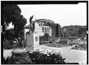 Exterior view of the San Juan Capistrano Mission, showing a garden and statue