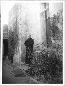 Franciscan priest standing on a lower step of a set of outside stairs at Mission Santa Barbara, 1898-1900