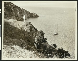 Man looking down at a small schooner from the bluff above