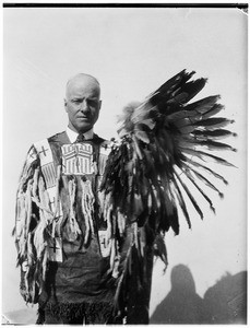 Man in traditional Native American dress, holding a headdress in his hand at the Pacific Southwest Museum