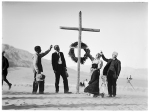 People pointing up at a cross at a funeral in the desert