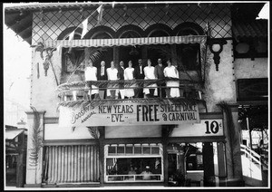 Portrait of people standing on a balcony above a sign advertising "The Booster's Annual New Year's Eve Free Street Dance and Festival" in Redondo Beach, 1926