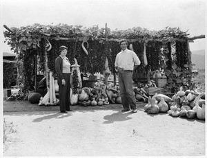 Portrait of a woman and man posing in front of a Pauma Indian fruit and vegetable stand, ca.1900