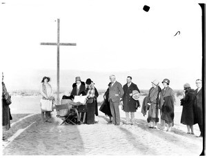 People looking inside a rectangular object near a cross for a funeral