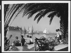 Six people sitting at the shore watching sailboats on the sea, ca.1940