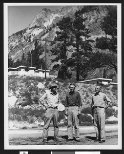 Portrait of three men standing on a road at the base of a mountain