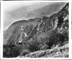 View of Mount Lowe Railway circular bridge in distance, overlooking a cliff with brushes and trees, from Sunset Point