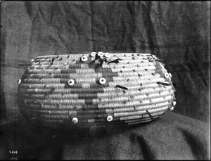 Indian basket displayed in front of a cloth backdrop, ca.1900