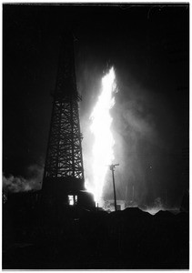 Oil geyser at an unidentified oil field, showing a derrick next to the fire