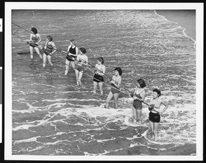 Women in bathing suits fishing while standing in the surf, ca.1930