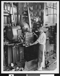 Close-up of a man working a machine inside an unidentified factory, ca.1935