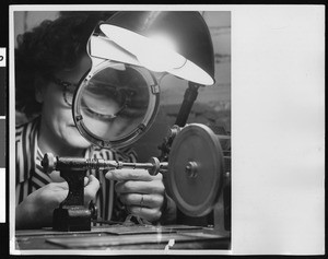 Close-up view of female factory worker examining a small metal component, ca.1940