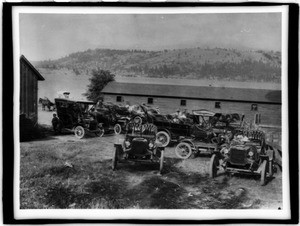 Automobiles parked near a long wooden a boat house adjacent to a lake in California, ca.1910