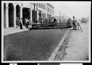 Workers using an asphalt finishing machine on an unidentified street