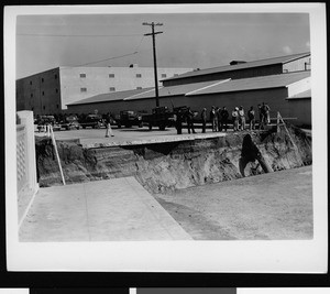 Flood damage to Warner Brothers Studio, showing men viewing a crevasse in the street, 1938