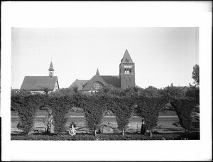 First and second buildings of Presbyterian Church, viewed through a cypress hedge, Santa Monica, ca.1898