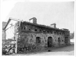 A dog sleeps on the ground in front of the Priests' residence of Mission San Luis Obispo de Tolosa, ca.1900