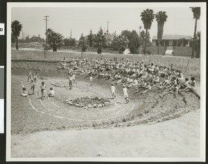 Small children running around a crude dirt track, 1932