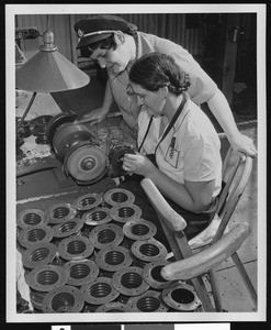 Two factory women workers examining cylindrical components, ca.1930