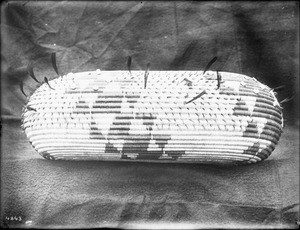 Indian basket displayed in front of a cloth backdrop, ca.1900