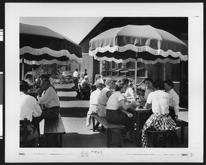 Group of employees sitting around shaded tables outside a building, ca.1950