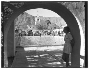 Woman standing in an archway in front of a swimming pool with mountains in the background