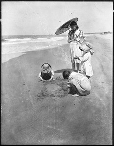 Children playing in the sand at the feet of a parasol-shaded woman at Newport Beach, ca.1920