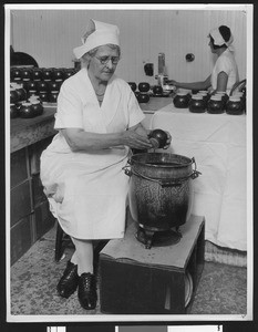 Woman worker sealing honey jars with beeswax, ca.1930