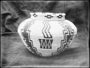 Indian basket displayed in front of a cloth backdrop, ca.1900