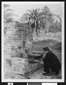 Man putting wood in an outdoor cookstove, ca.1930