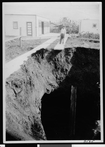 Man standing near a deep sinkhole near a house