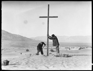 Two men erecting a cross in the sand for a funeral in the desert