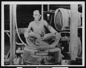 Factory worker manipulating a tube tire with machinery, ca.1930