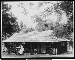 People relaxing in front of a cabin, ca.1910