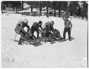 Three people being pushed down a hill on toboggans at Big Pines